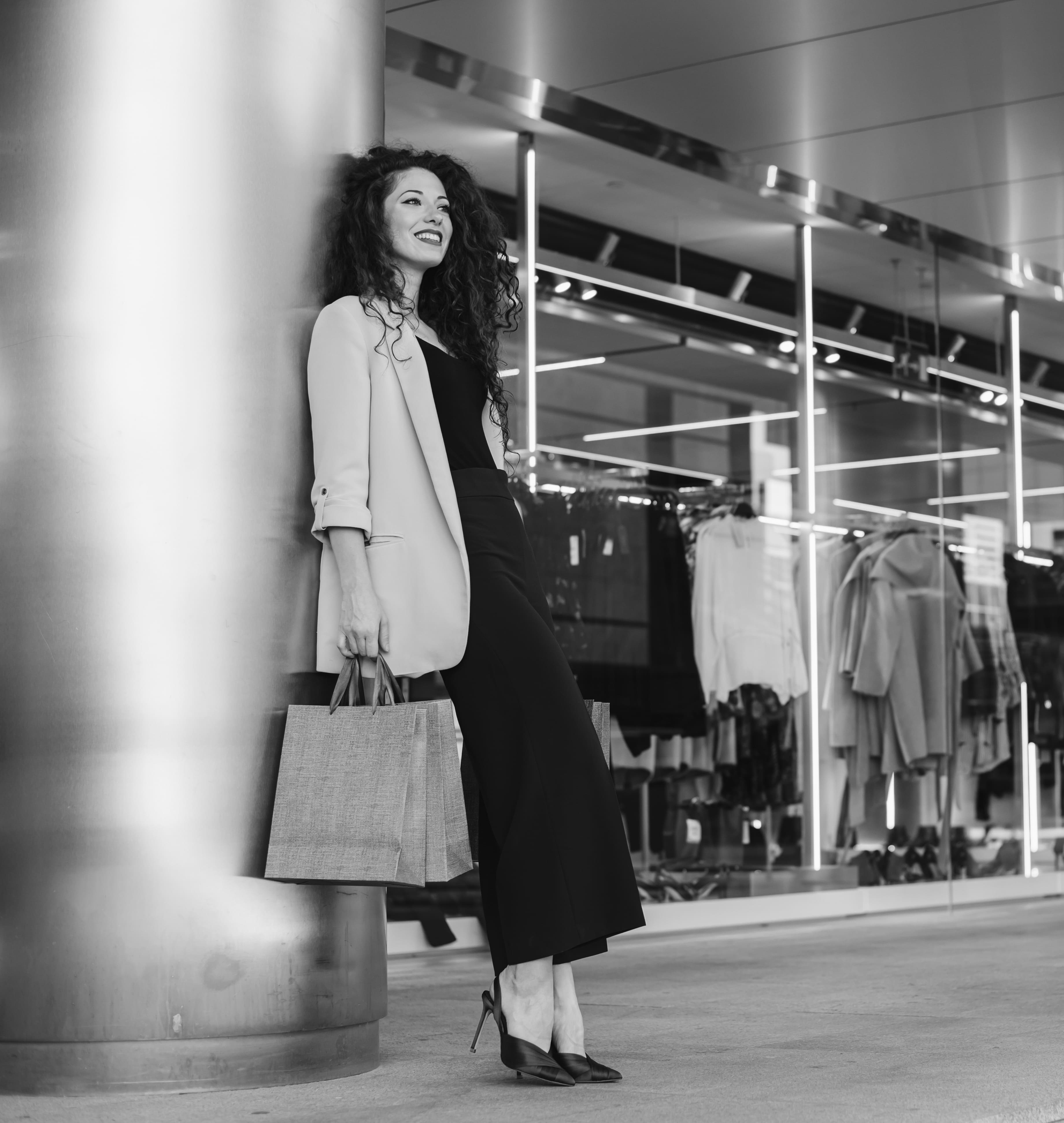 Woman with shopping bags leaning against a pillar outside a storefront