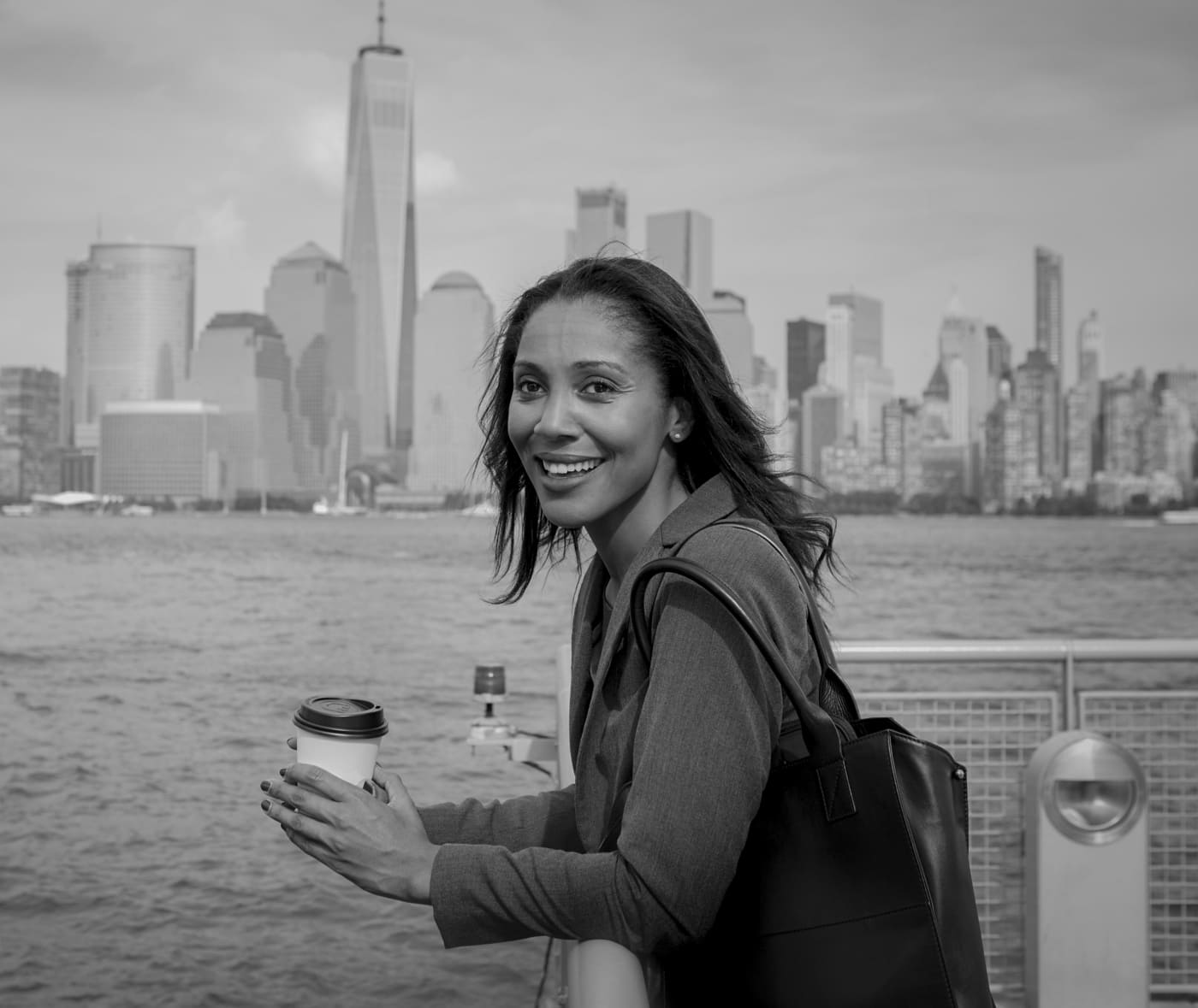 Smiling woman with coffee on a ferry with the Manhattan skyline behind her